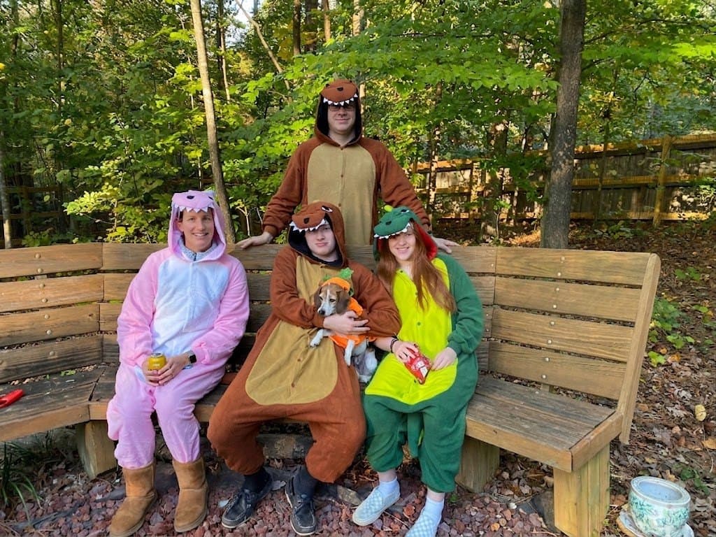 Scott Hall with his family and dog, all in dinosaur onesies, on a bench in the woods